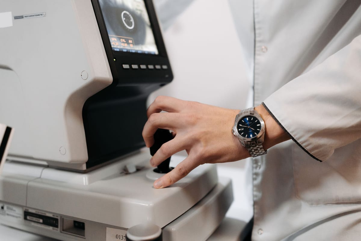 A clinician's hand operating a ref/keratometer during an eye examination